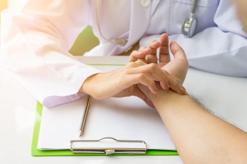 Doctor is checking patience's pulse by fingers, medical checking on table. Asian doctor